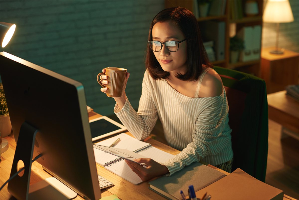 Mulher a trabalhar ao computador à noite, com uma caneca de café na mão — a cafeína tardia que rouba horas de sono