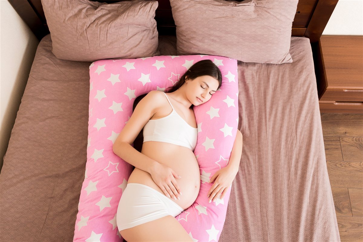 Grávida a dormir de lado, confortável, com uma almofada de gravidez de apoio ao corpo