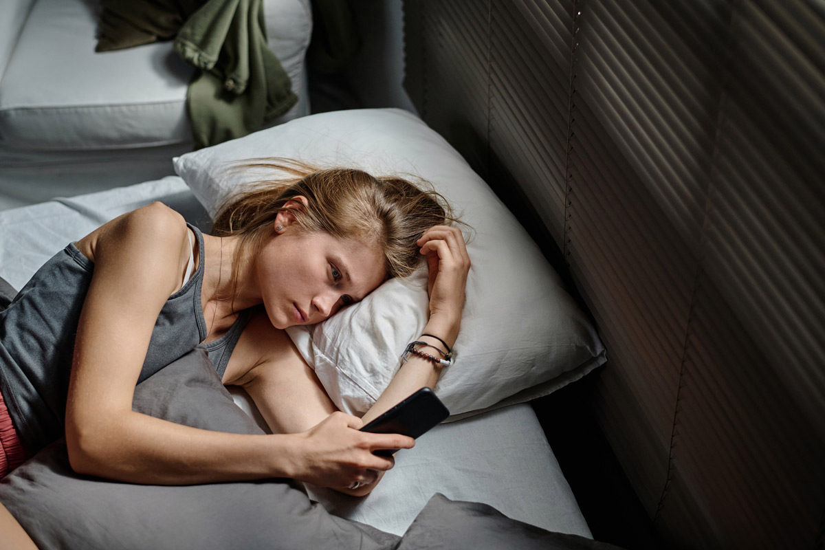 Jovem ansiosa a olhar para o telemóvel à noite, sem conseguir dormir