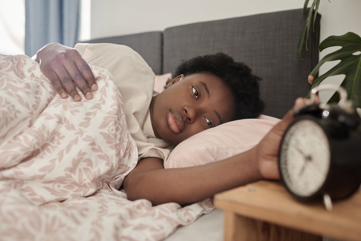 Mulher deitada na cama, ainda ensonada, a desligar o despertador
