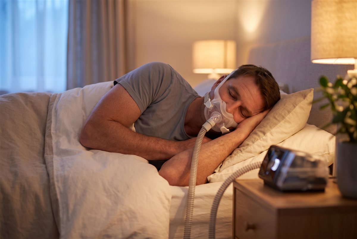 Homem a dormir tranquilamente de lado, já com a máscara de CPAP colocada, expressão calma
